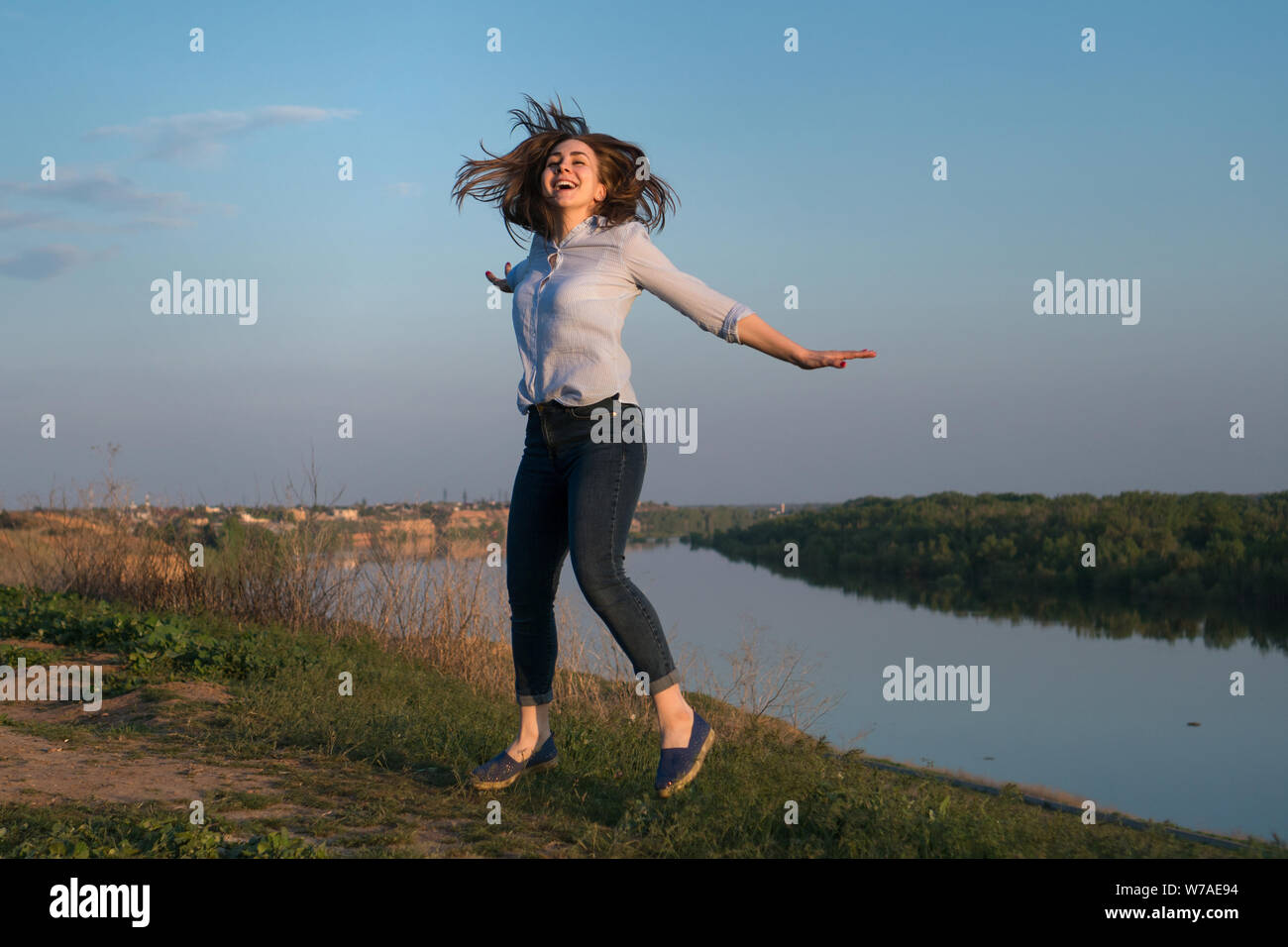 Shapely ragazza jocund ballare sulla natura dello sfondo. Di buon umore lady jumping con sorriso. Foto Stock