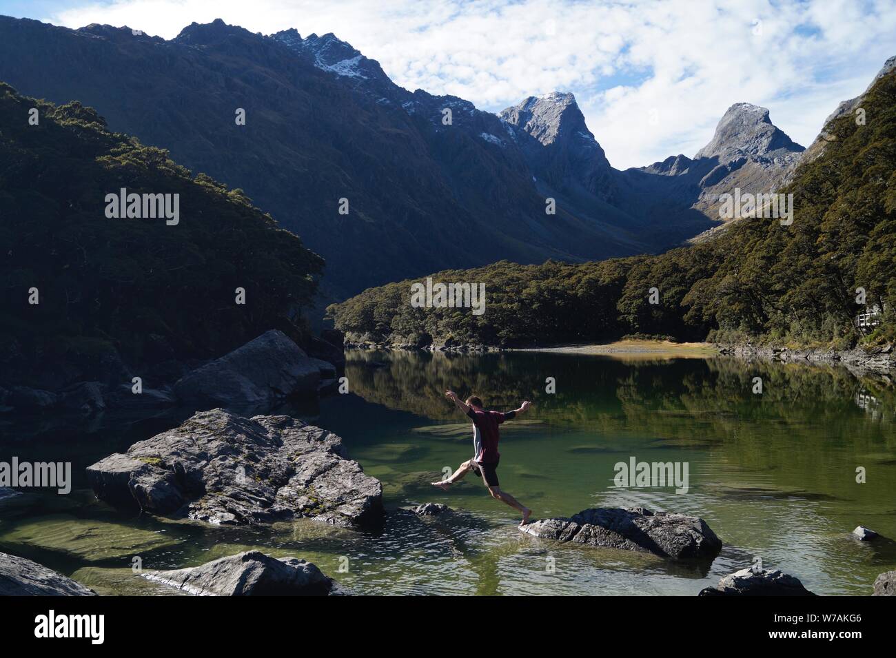 L'uomo salti attraverso le rocce su un verde lago blu Foto Stock