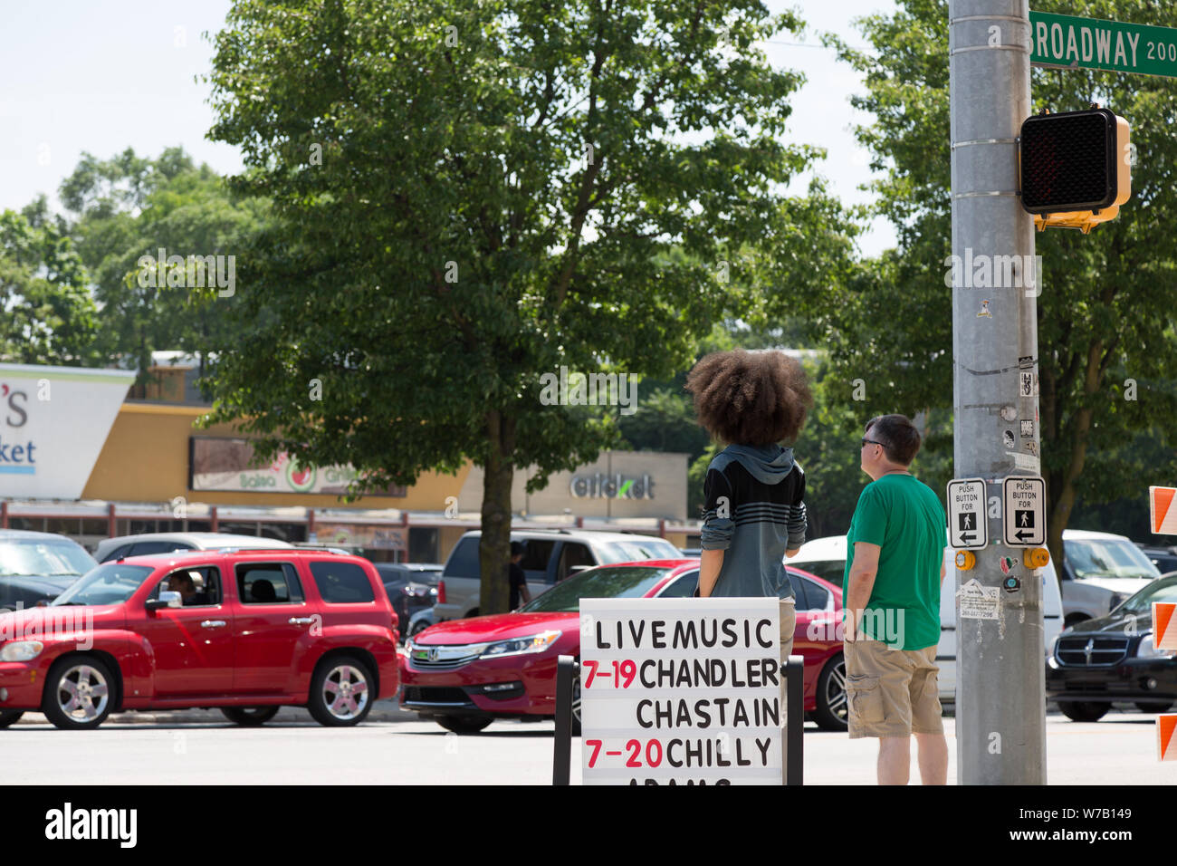Un uomo si erge accanto ad un adolescente con un grande Afro come sono in attesa in un angolo della Taylor Street e Broadway a sud del centro di Fort Wayne, Indiana, Stati Uniti d'America. Foto Stock