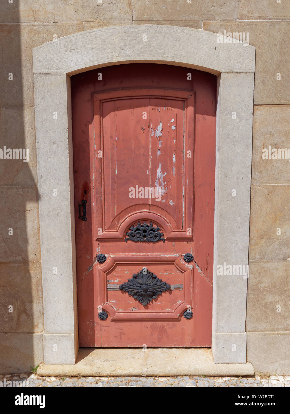 Una porta di legno con sbiadito e Peeling vernice rossa, con altamente decorato porta di metallo insieme di mobili in una parete nei giardini del palazzo di Estoi in Portu Foto Stock