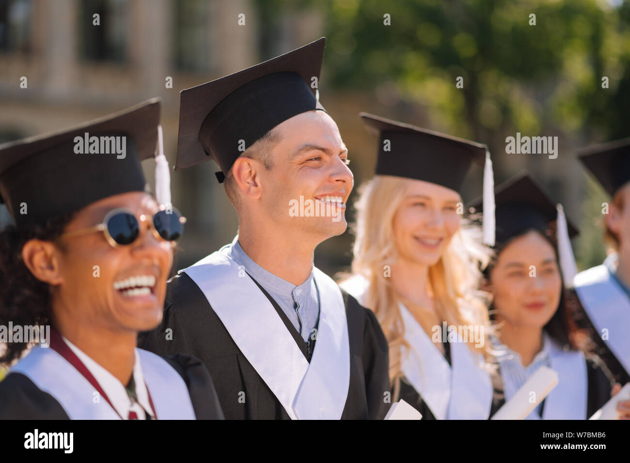 Ragazzo sorridente in piedi tra i suoi amici durante la cerimonia di laurea. Foto Stock