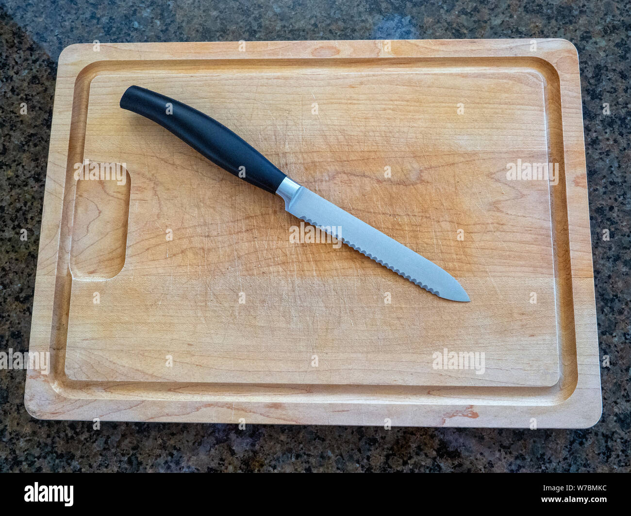 Vista dall'alto di un isolato utility seghettata coltello su un grande tagliere di legno con una cucina di granito contatore sfondo superiore Foto Stock