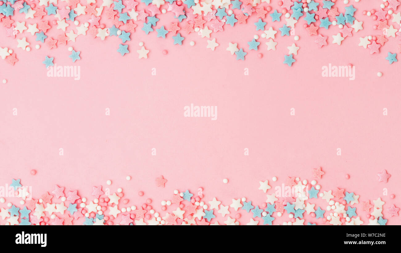 Cornice di confine festosa di colori pastello spruzzi su sfondo rosa con spazio copia al centro. Spolverare i punti e le stelle dello zucchero, la decorazione per la torta e la panetteria. Vista dall'alto o piatta. Banner Foto Stock