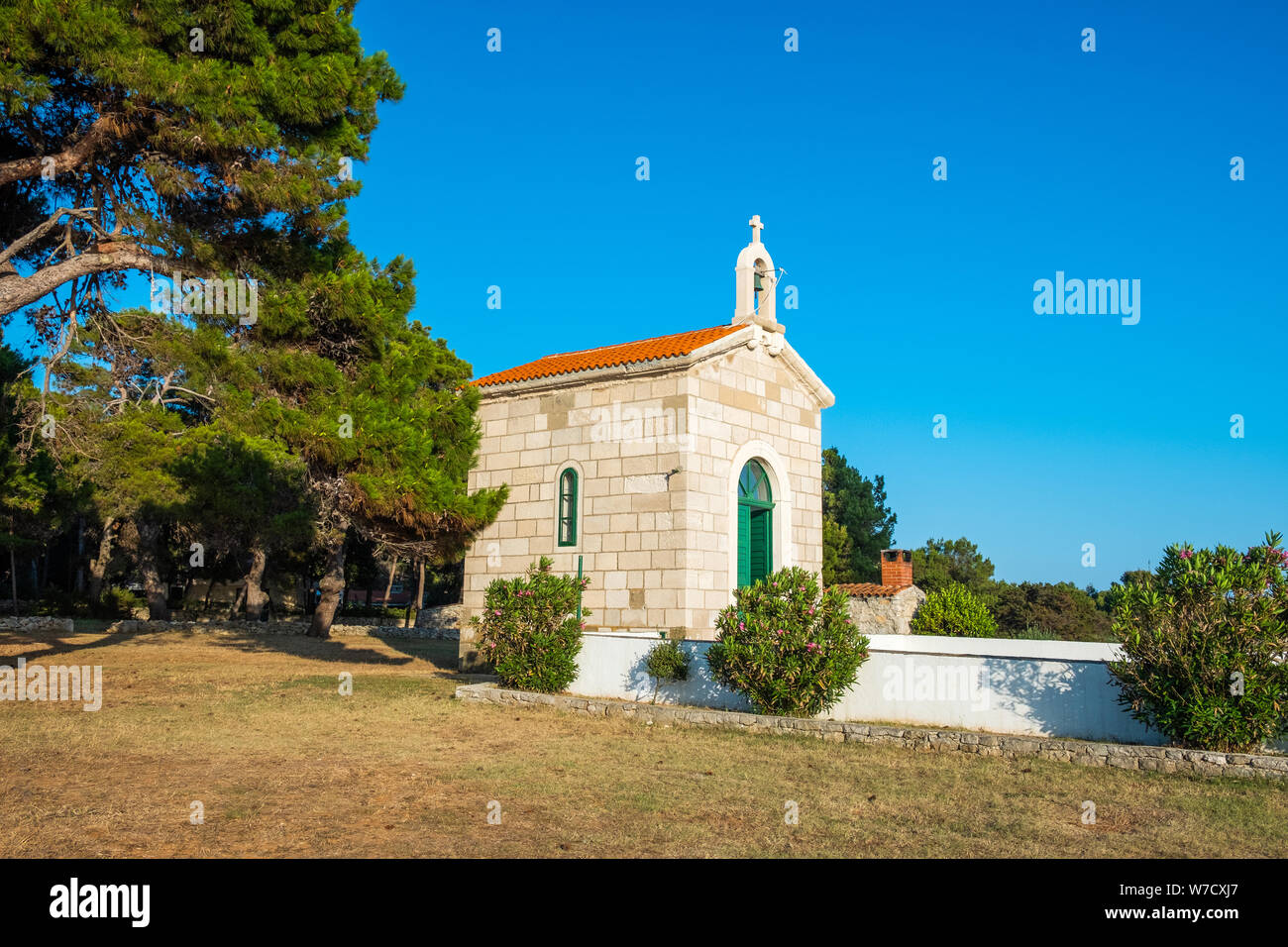 Croazia, isola di Dugi Otok, bella e antica chiesa in pietra di Veli Rat sulla pietra a riva tra i pini sulla giornata di sole, paesaggio mediterraneo Foto Stock