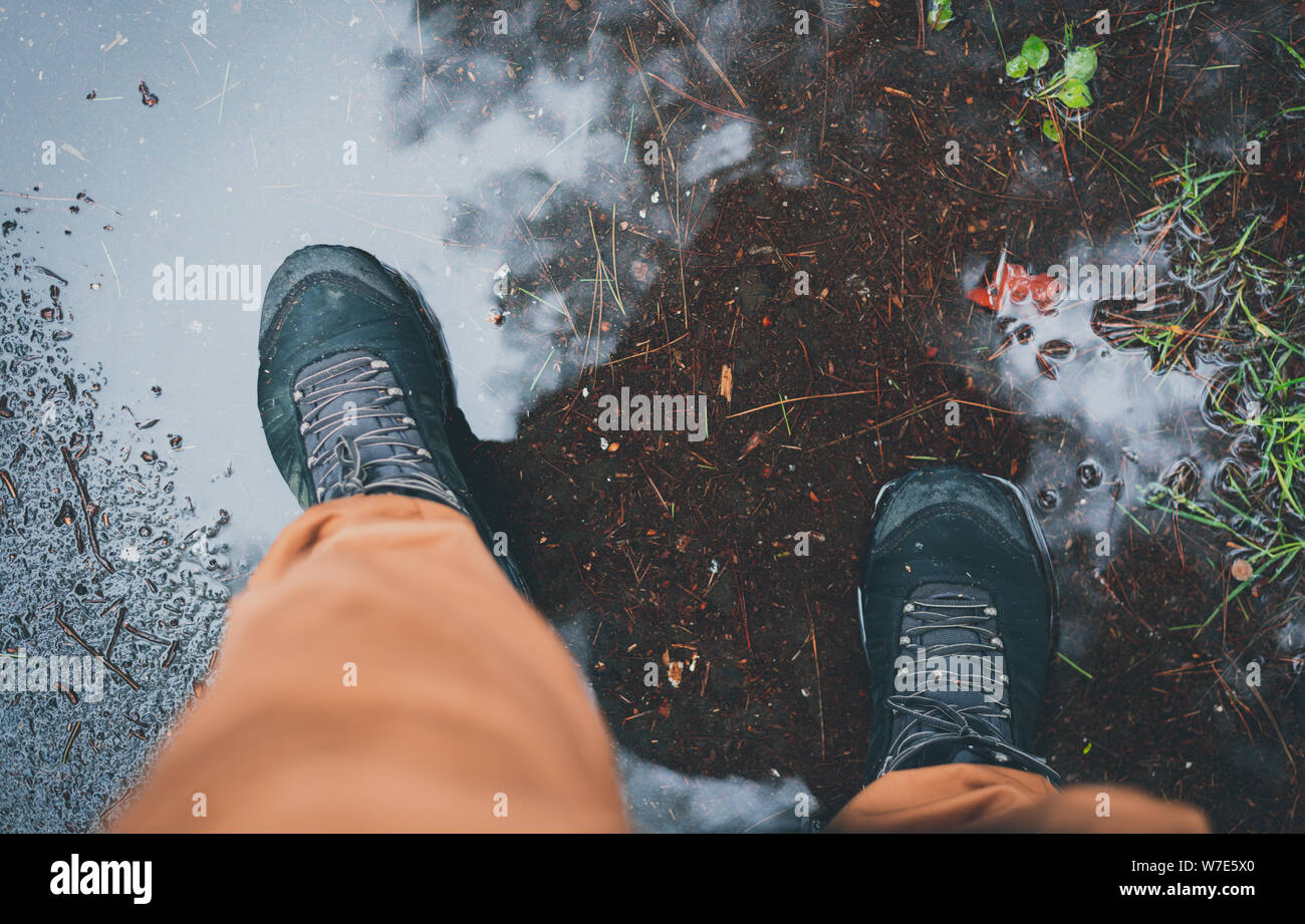 L'uomo staingg durante il piovoso autunno Meteo in una pozza in un impermeabile scarpe tracking. Tempo di caduta del concetto. Tutta la stagione adventure concept. Backgrou fangose Foto Stock
