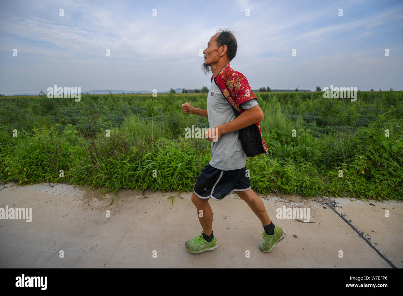 (190806) -- CHANGCHUN, il 6 agosto 2019 (Xinhua) -- alto e sottile, con un ovvio di barba e un impressionante e fiorito di cotone imbottito camicia rossa, 63-anno-vecchio Xi Zhanyu tagliare una cifra distintiva in esecuzione nel campo nelle zone rurali Taku Village, vicino la Cina del nord-est della città di Changchun. "I vestiti apparteneva a mia moglie tardiva Xia Shuyun. Volevo correre con lei.' Xi ha detto. Nel 2015, Xia è stato diagnosticato un cancro ai polmoni. Quando morì, Xia sentito aveva ancora molto da realizzare. "Poi ho iniziato a vedere se mi apporterebbe qualsiasi comodità," ha detto. Da allora in poi, ogni giorno, o la pioggia, gli abitanti di un villaggio sarebbe vedere Foto Stock