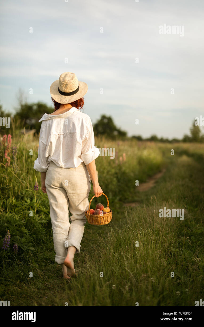 Un lato del paese ragazza camminare lungo il sentiero con un cesto di pesche Foto Stock