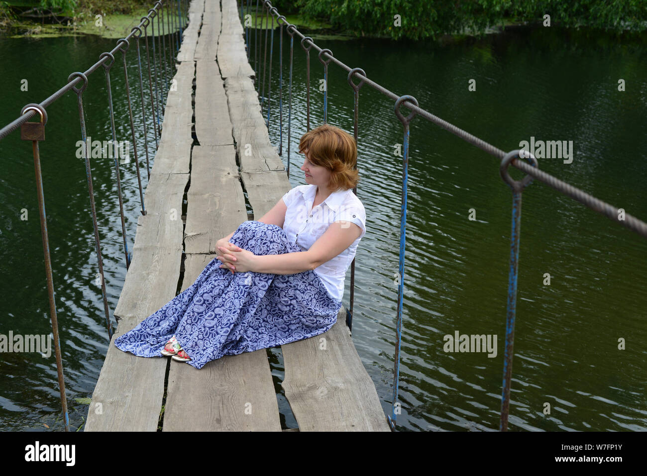 Donna seduta su un ponte in legno sul fiume Foto Stock