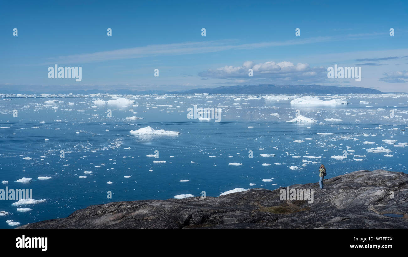 Un turista guardando alla baia di Disko con blocchi di ghiaccio provenienti da Ilulissat fiordo di ghiaccio, vicino a Ilulissat in Groenlandia occidentale. Foto Stock