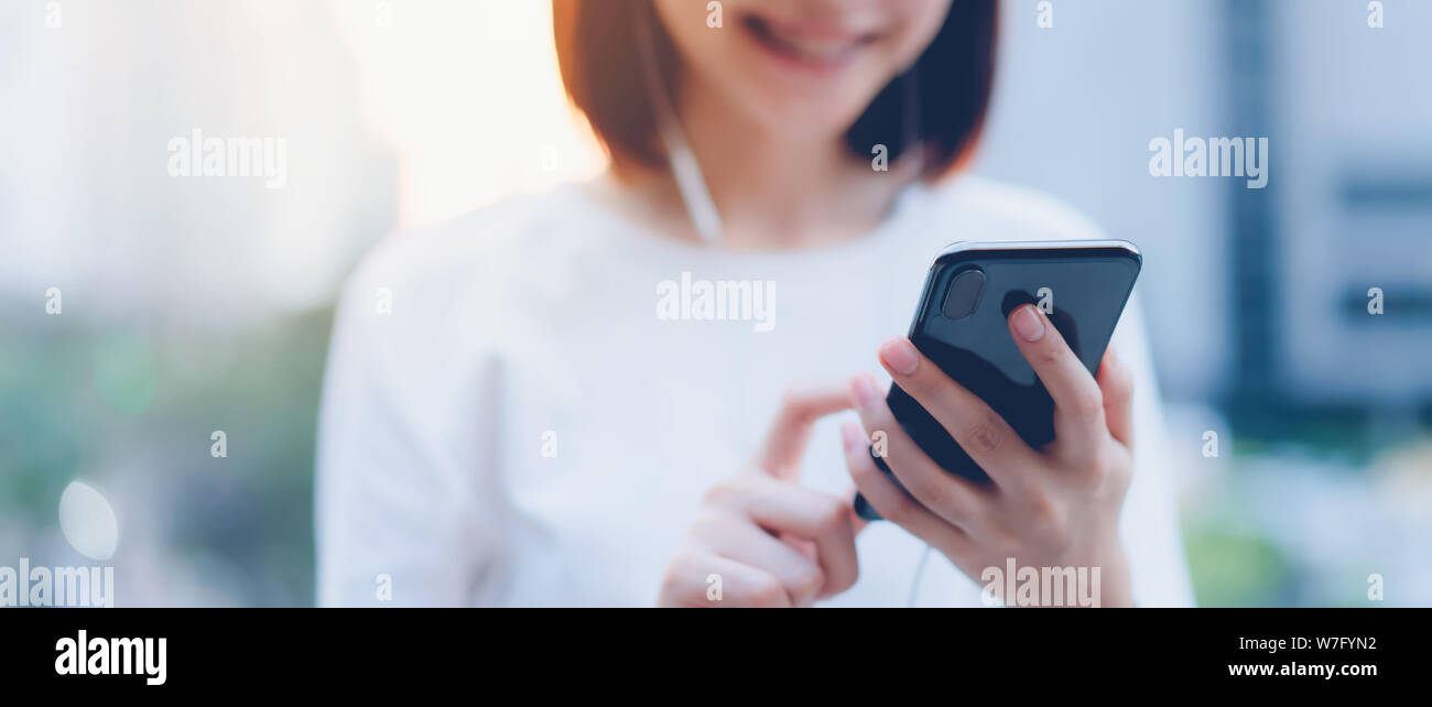 Sorridente donna asiatica utilizza lo smartphone con l'ascolto di musica e di stare in ufficio. Foto Stock