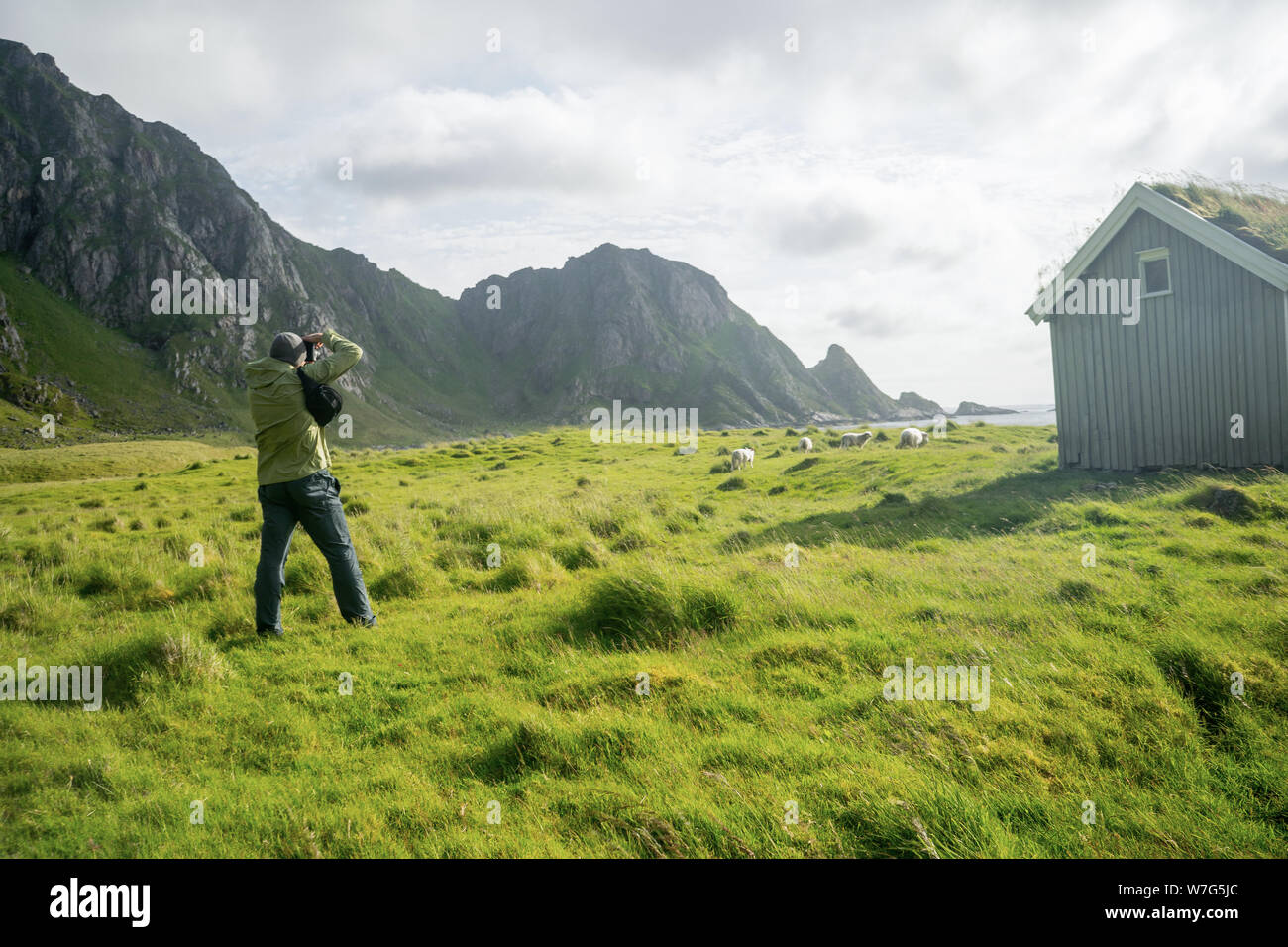 Fotografo uomo che fotografa la tipica casa norvegese con erba sul tetto. Bella casa di villaggio colorato. Concetto di viaggio e hobby. Foto Stock