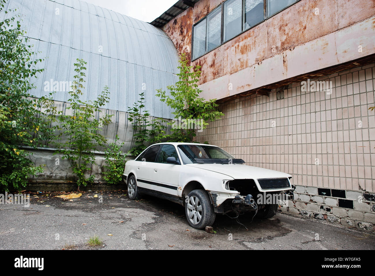 Bianco auto smontato senza fari anteriori, paraurti e egine alla vecchia fabbrica. Foto Stock
