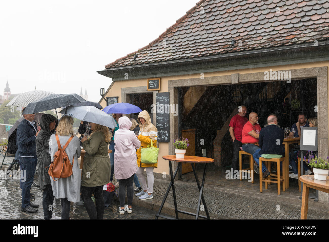 Le persone aventi un drink sotto la pioggia all'aperto con Ombrello e soprabito impermeabile a Würzburg, Germania Foto Stock