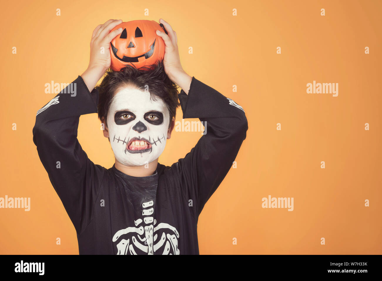 Happy Halloween.divertente bambino in un costume di scheletro con zucca di Halloween sulla sua testa contro lo sfondo arancione Foto Stock