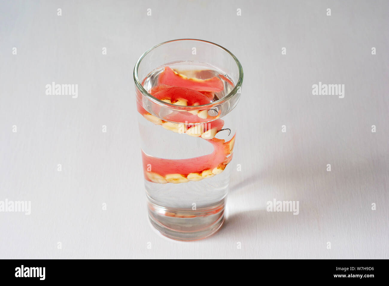 Dentiera in un bicchiere con acqua su uno sfondo bianco. Foto Stock