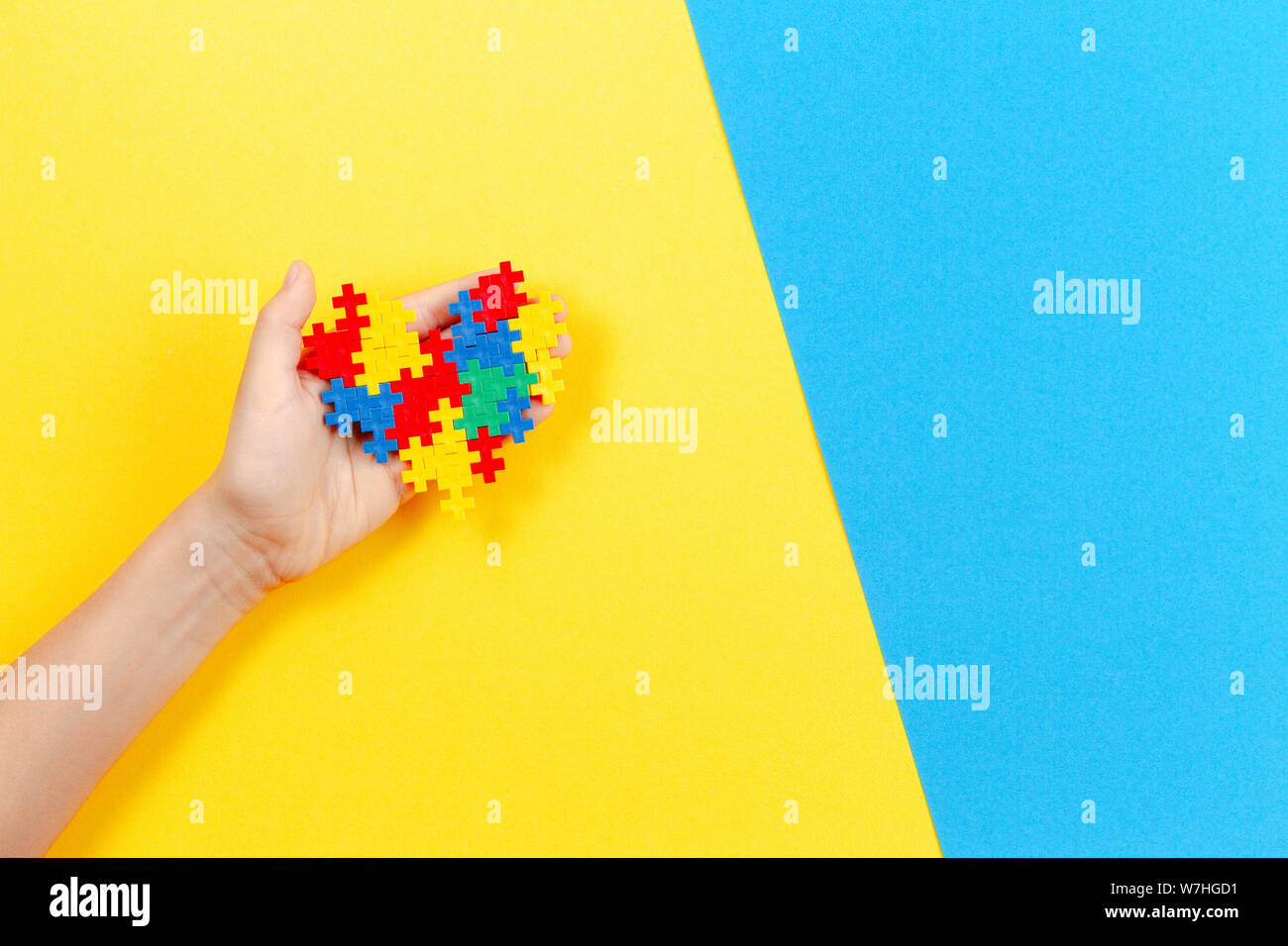 Kid mano azienda cuore colorati in giallo e blu sullo sfondo. Mondo autismo consapevolezza giorno di concetto Foto Stock