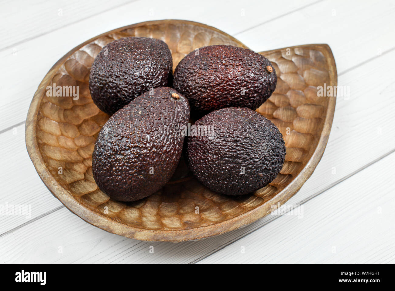 Il marrone scuro avocadi ( bilse varietà ) su legno scolpito ciotola. Foto Stock