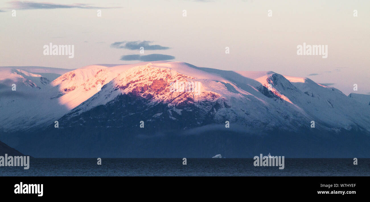 Iceberg sfuggire al sun di raggi di fusione, sopraffatte dal ghiaccio circostante-capped mountains. Foto Stock