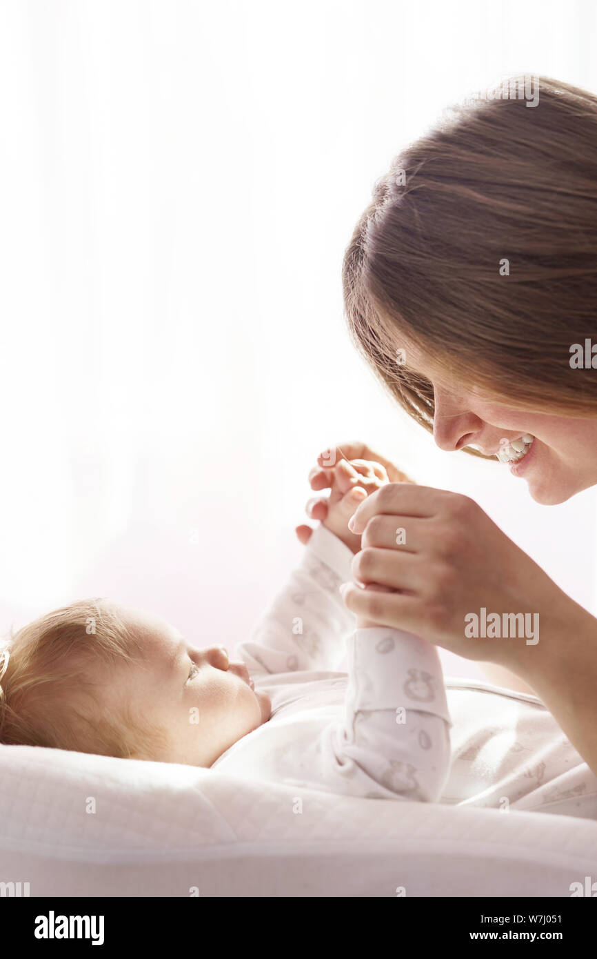 Un neonato è sdraiato sul letto e la madre si tiene le mani Foto Stock