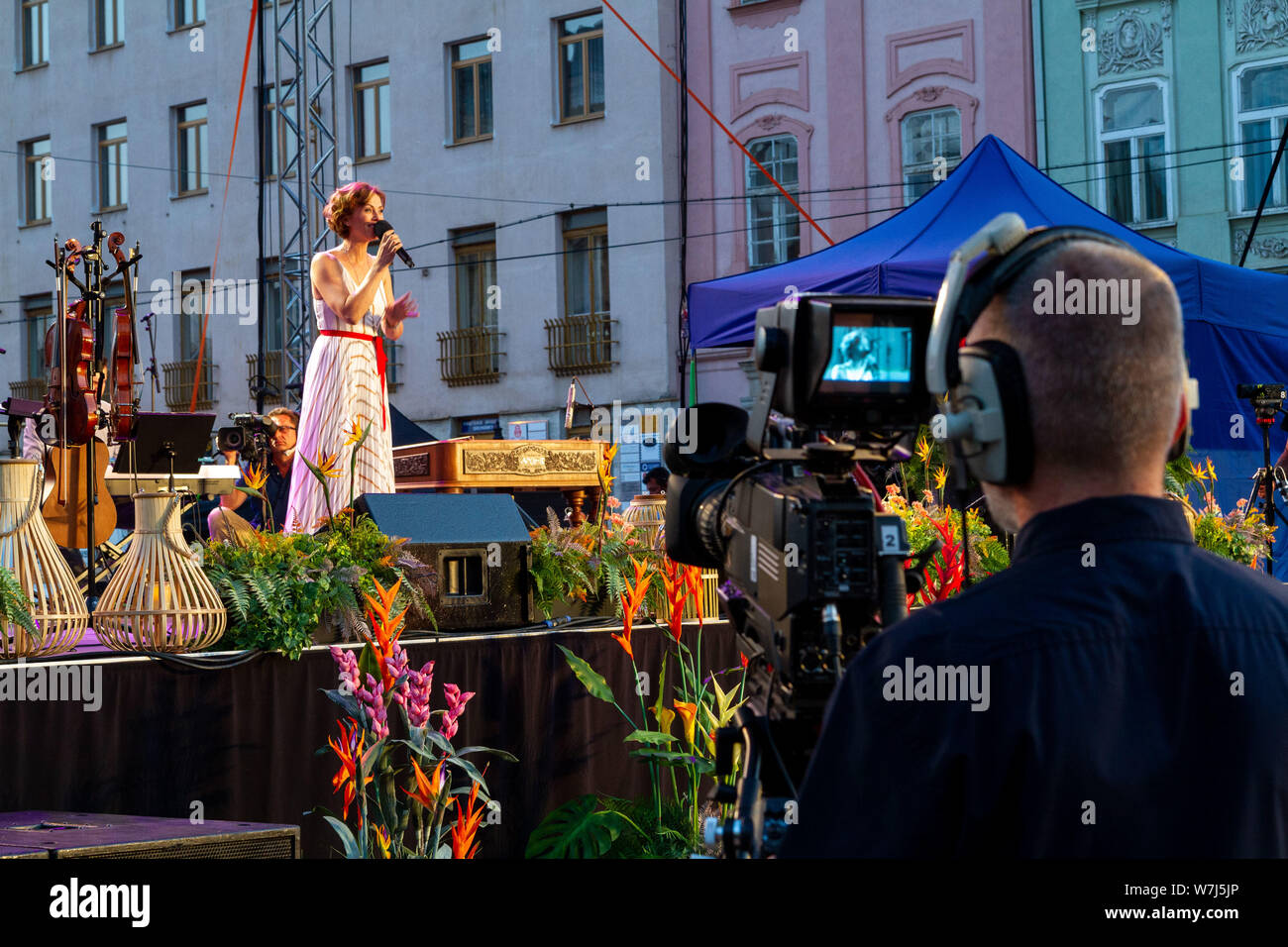 Un cantante di cantare su un palcoscenico all'aperto durante un concerto di beneficio. Un cameraman è ripresa l'evento dal vivo. Foto Stock