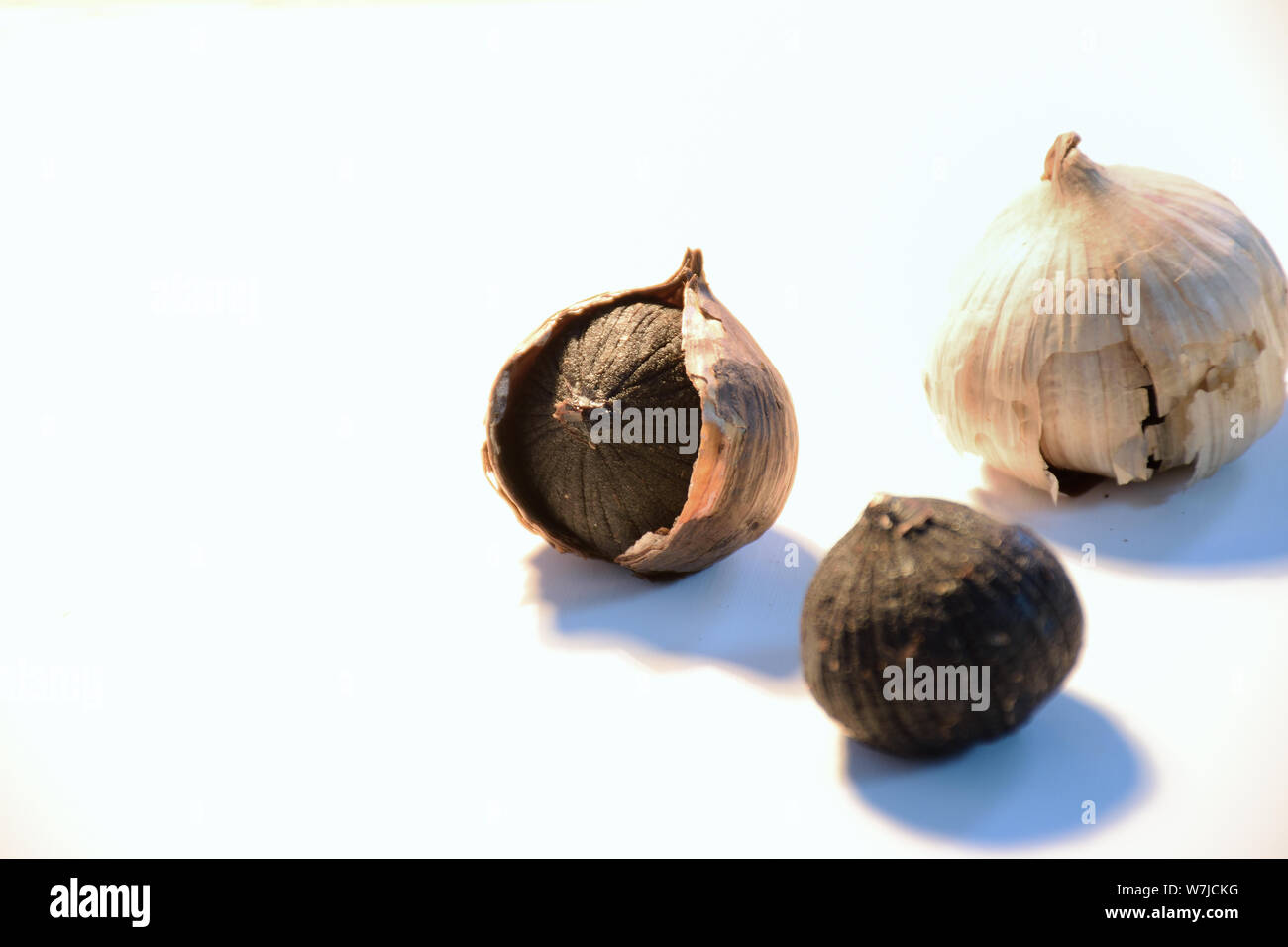 3 pezzi di aglio nero con uno sfondo bianco in un tono caldo. Uno di loro con la buccia su, uno con la scorza di mezzo e uno senza buccia. Foto Stock