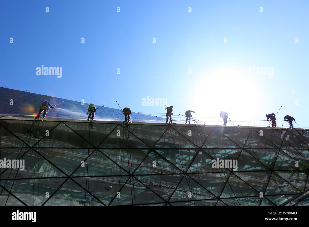 Cinese i lavoratori migranti a penzolare da corde per pulire i 25.000 metri quadrati di parete esterna della Shengjing Grand Theatre per salutare il prossimo Shenyang Foto Stock