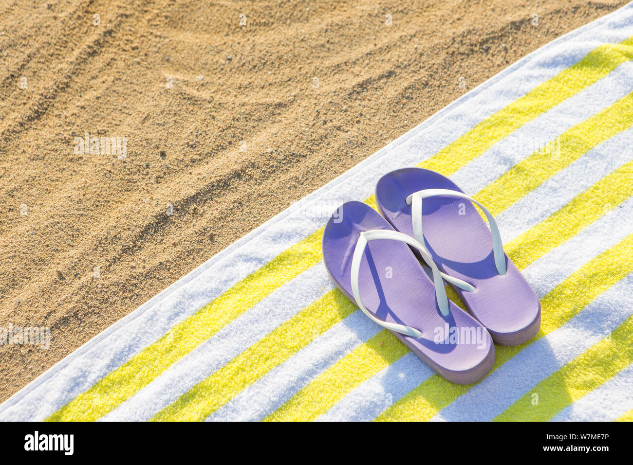 Pantofole viola sul tovagliolo giallo su sfondo di spiaggia Foto Stock