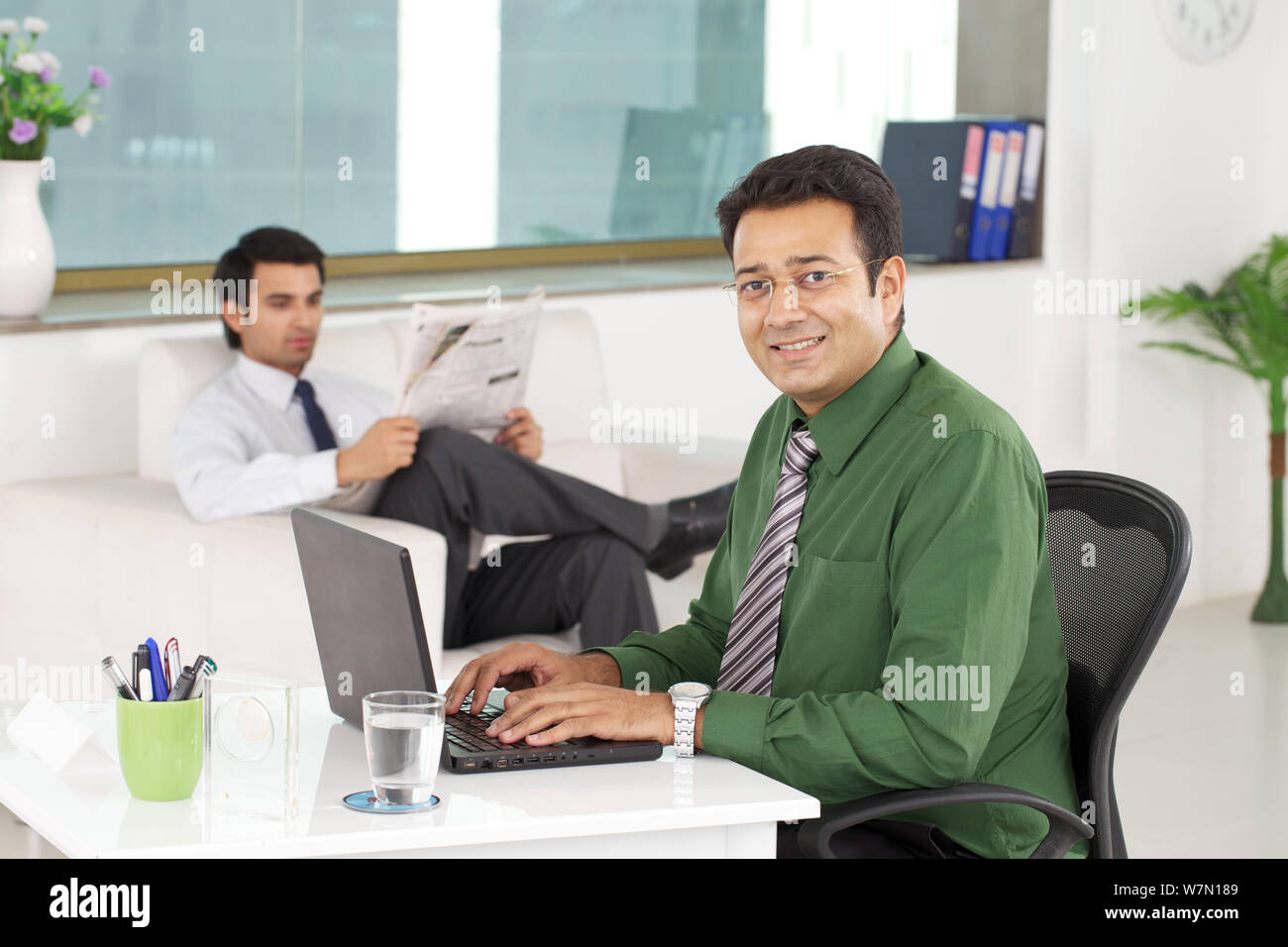 Consulente finanziario che lavora su un notebook con un cliente in attesa sullo sfondo Foto Stock
