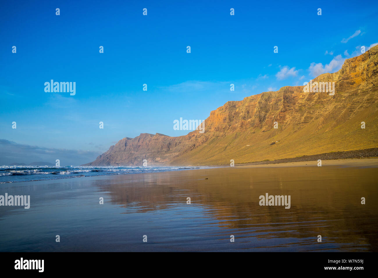 Spagna, Lanzarote, popolare spiaggia di surf Famara riflettendo impressionanti montagne di famara Foto Stock