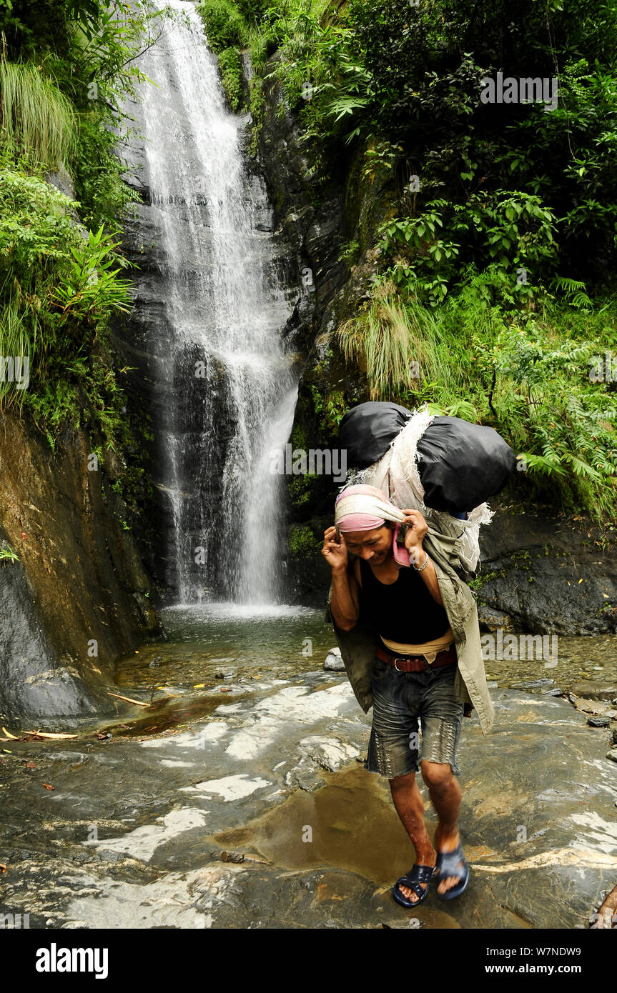 Portiere caricato nel Budhi Gandaki sulla valle del fiume a piedi attraverso il fiume con cascata dietro, Il Manaslu Area di Conservazione, Himalaya, Nepal, ottobre 2009. Foto Stock
