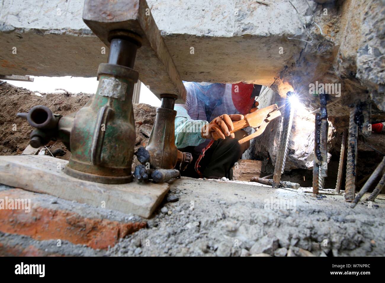 Un lavoratore cinese rafforza l'edificio a quattro piani di fondazione tramite la saldatura delle barre di acciaio e la colata di cemento dopo lo spostamento della costruzione di 10 metri Foto Stock