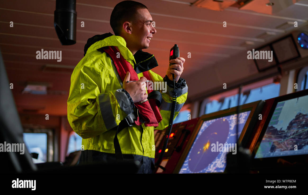 Navigator. pilota, capitano come parte dell equipaggio della nave di eseguire incarichi giornalieri con la radio VHF, binocolo, giornale di bordo, in piedi vicino a ECDIS e stazione radar Foto Stock