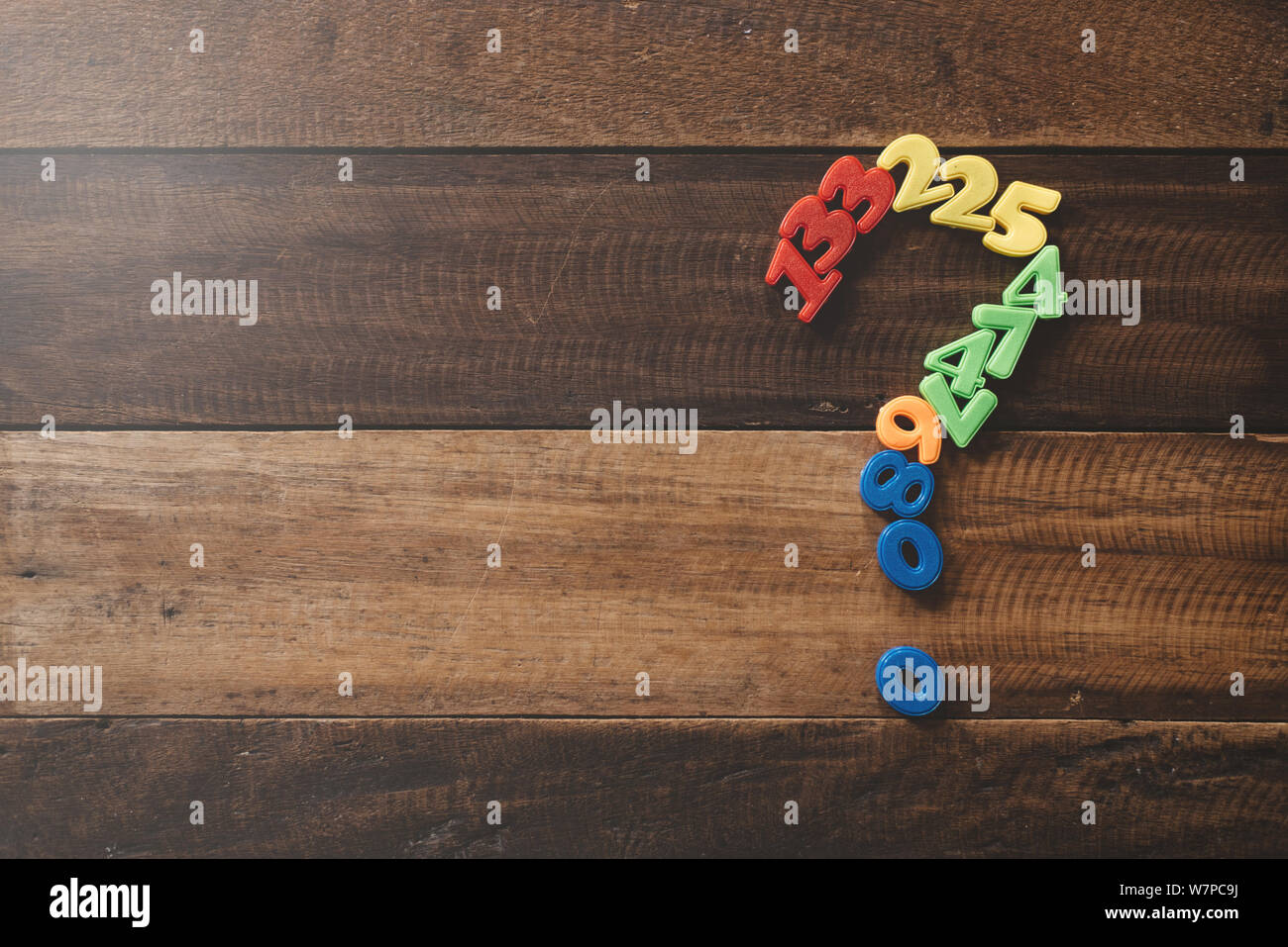 Gruppo del giocattolo di plastica formando i numeri di punto interrogativo su di un tavolo di legno. Concetto di domande, faq e i problemi matematici Foto Stock