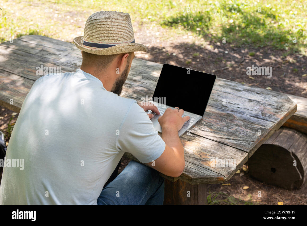 Uomo o ragazzo lavorando su un computer con uno schermo vuoto per copiare lo spazio, seduta su una panchina in estate all'aperto in un parco. vista posteriore dalla spalla Foto Stock