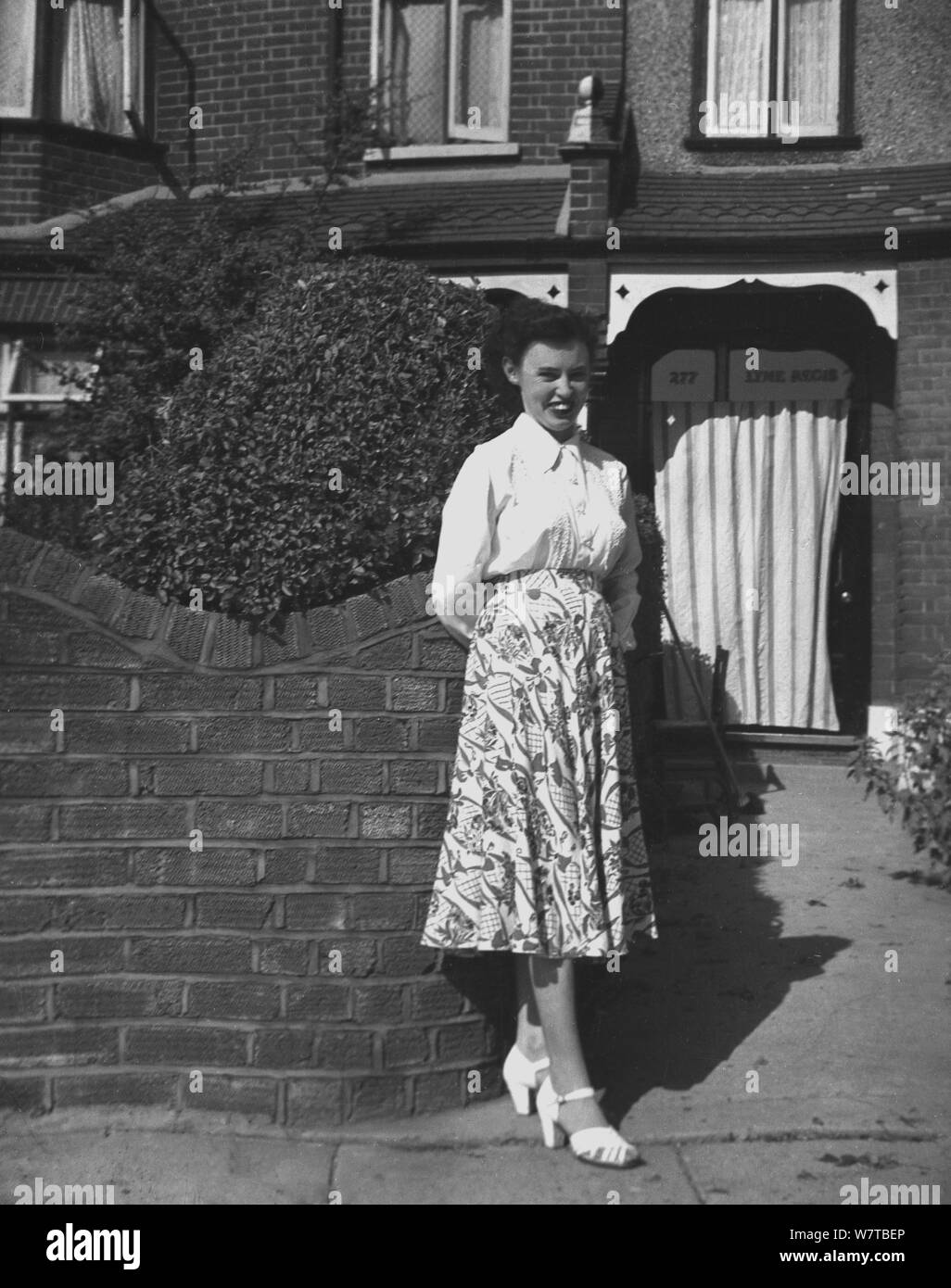 1951, storico, lady in piedi al di fuori di una guest house di Seely Rd, Lyme Regis, England, Regno Unito, con una tenda tirata sopra la porta anteriore. Foto Stock