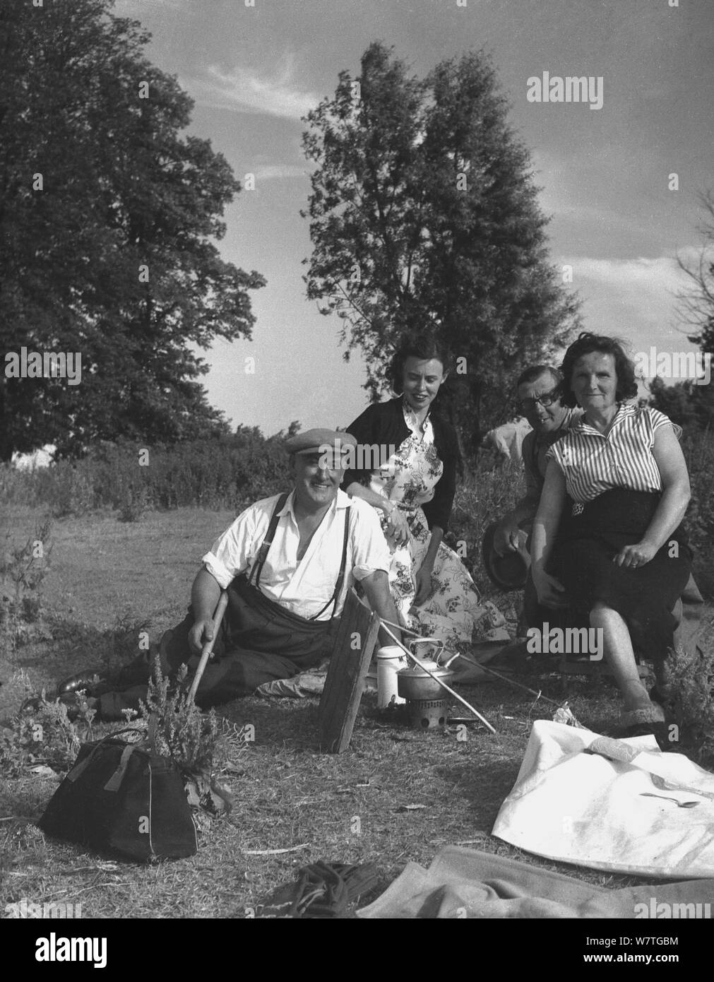 1950, storico, raccoglitrici di luppolo e la famiglia ai visitatori al di fuori seduta insieme con una birra da un fuoco di campo dopo una giornata nei campi, Kent, Inghilterra, Regno Unito. Foto Stock
