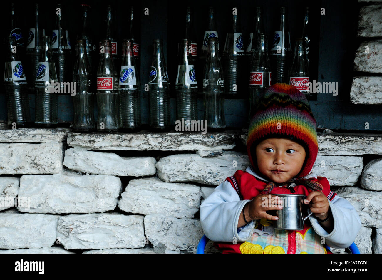 Un bambino di bere da parete con vuoti di bottiglie di vetro, nel piccolo villaggio di Khumnu. Santuario di Annapurna, centrale del Nepal, novembre 2011. Foto Stock