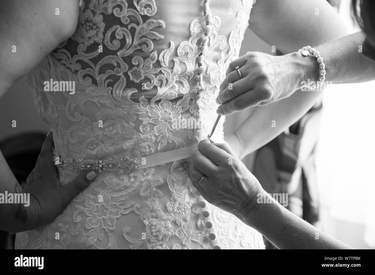 Spose abito essendo effettuato fino il giorno delle nozze, lacey abito nuziale essendo abbottonata fino pronto per la sposa di sposarsi il giorno delle nozze in Inghilterra Foto Stock