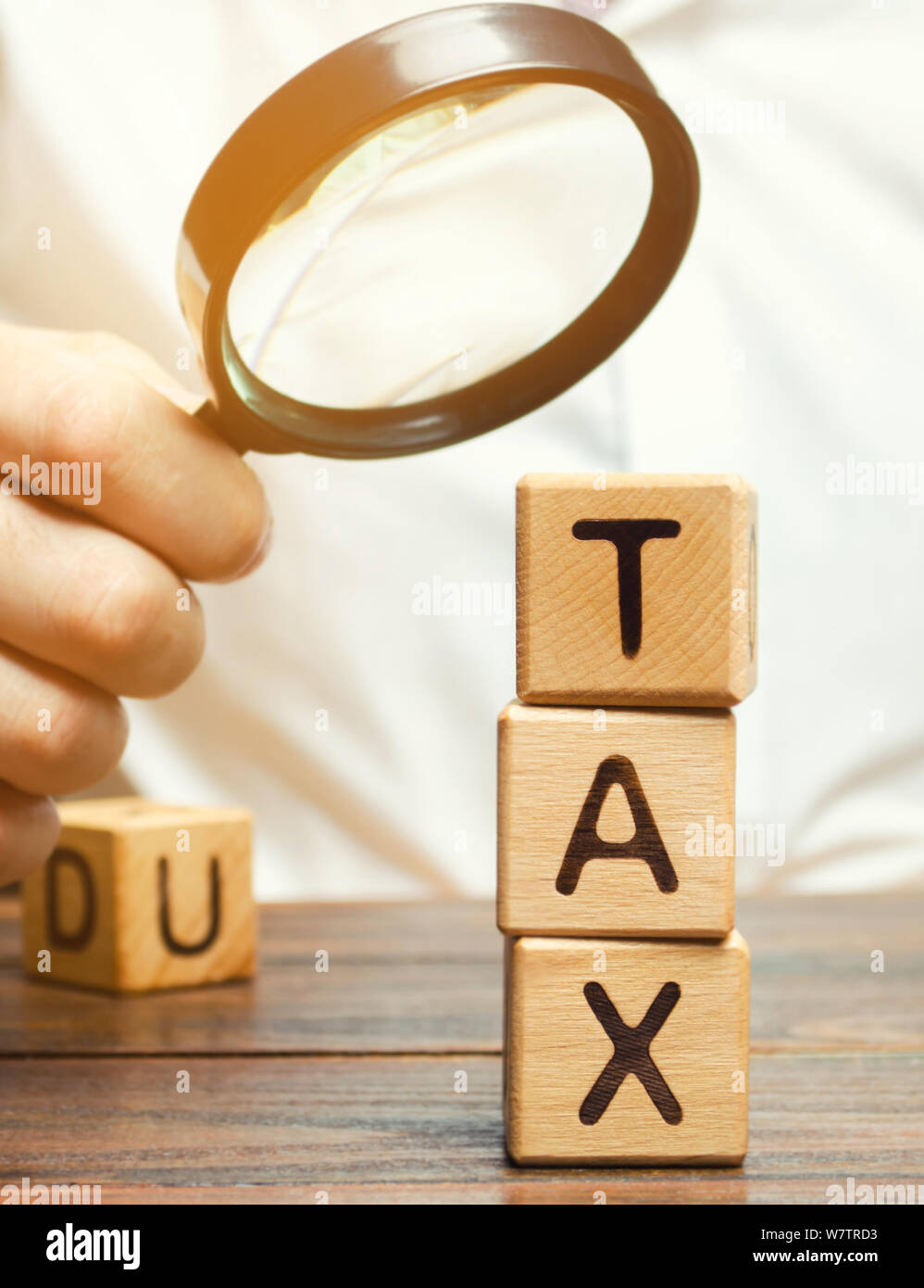 Blocchi di legno con la parola fiscale e di una lente di ingrandimento nelle mani di un imprenditore. Il concetto di studiare la dimensione delle imposte. Imposizione fiscale. Il termine di pagamento Foto Stock