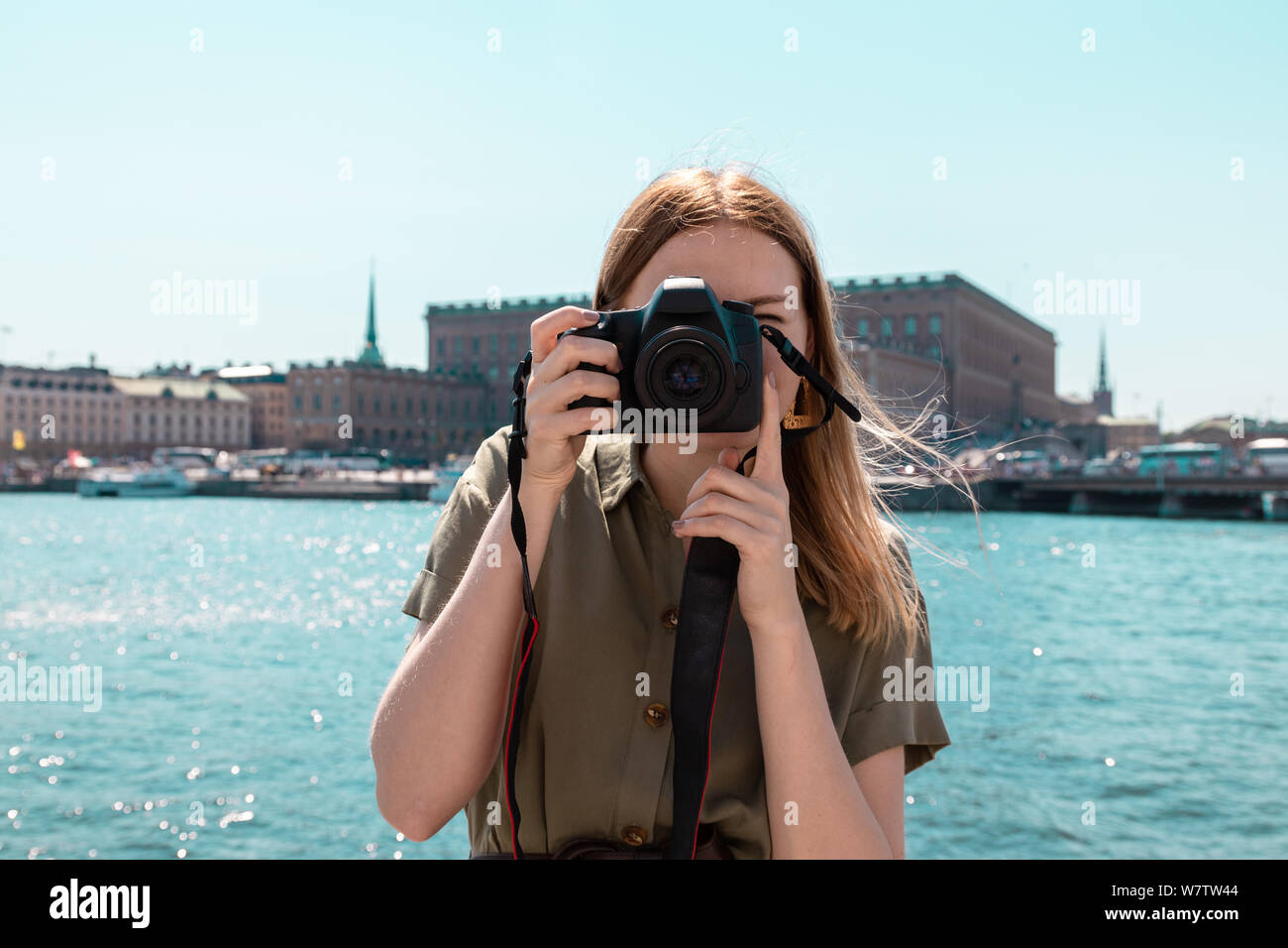 Viaggio concetto di viaggio. Turis bionda ragazza in una luce abiti estivi di colore verde contiene una telecamera e fotografie la città e sullo sfondo la sto Foto Stock