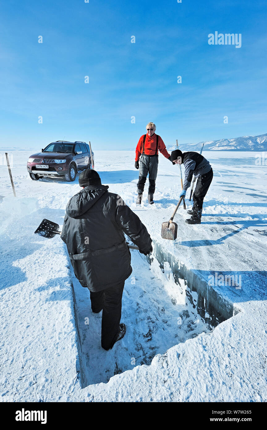 La gente di scavare un foro quadrato tramite thick Lago Baikal ghiaccio per immersioni sotto il ghiaccio, il lago Baikal, Siberia, Russia, Marzo. Foto Stock