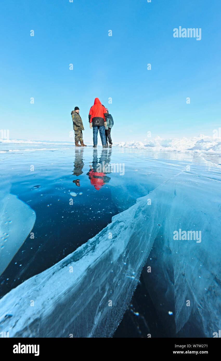 Persone in piedi su uno spesso strato di ghiaccio del Lago Baikal vicino al grande crack in ghiaccio, Lago Baikal, Siberia, Russia, Marzo. Foto Stock