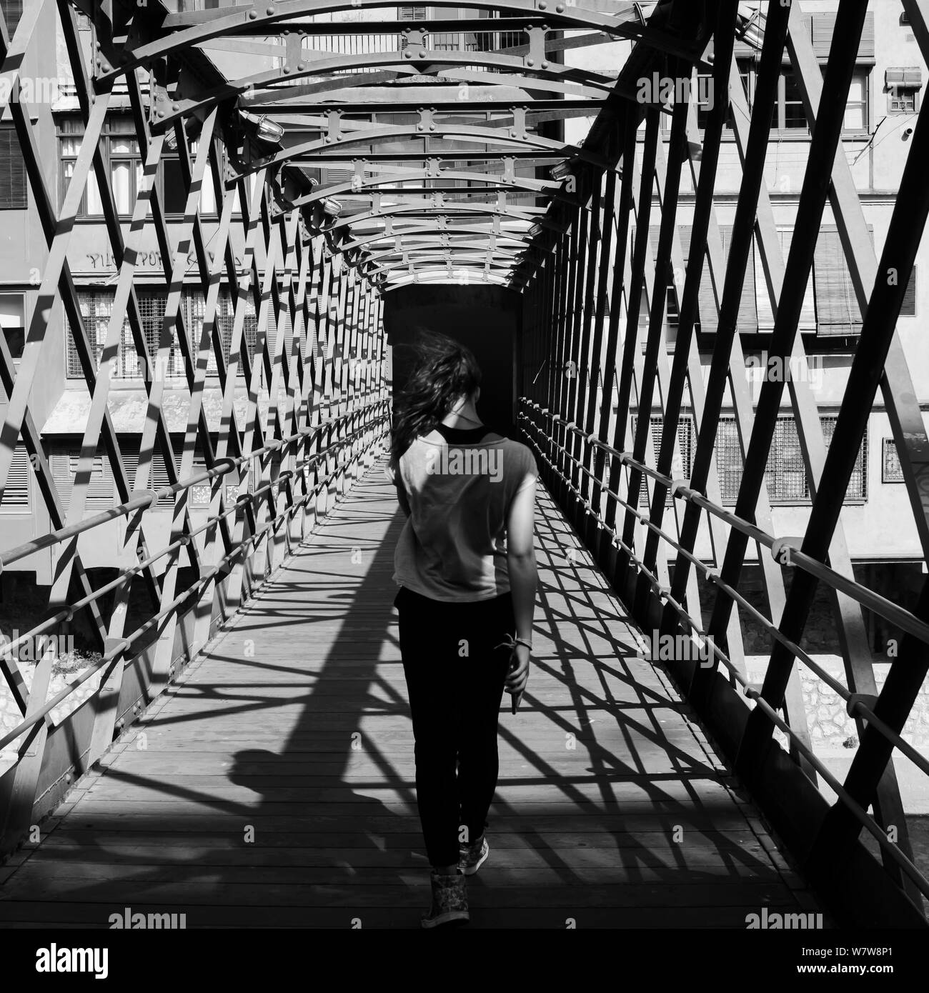 Vista posteriore di una giovane ragazza con i capelli svolazzanti attraversando a piedi il Pont de les Peixateries Velles, costruito da G. Eiffel in Girona, in Catalogna, Spagna Foto Stock