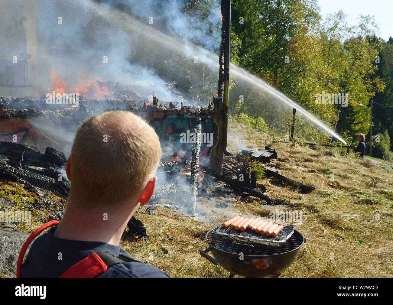 I vigili del fuoco di estinzione incendi controllati in casa abbandonata durante l'esercizio mentre un altro è in appoggio e di cuochi salsicce su un barbeque, Akerhus, Norvegia, settembre 2013. Foto Stock