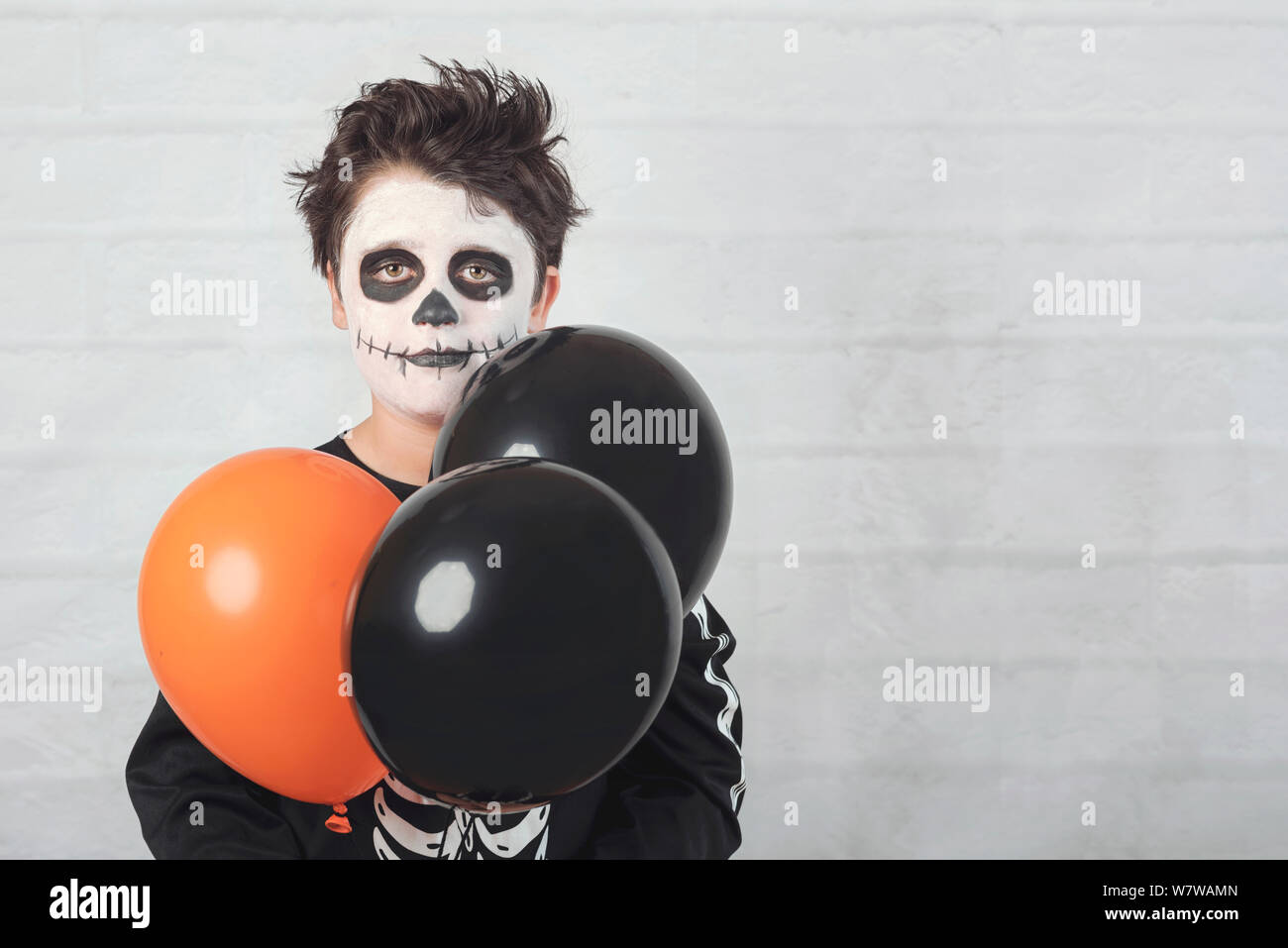 Happy Halloween. divertente bambino in un costume di scheletro con palloncini colorati contro Sfondo mattone Foto Stock