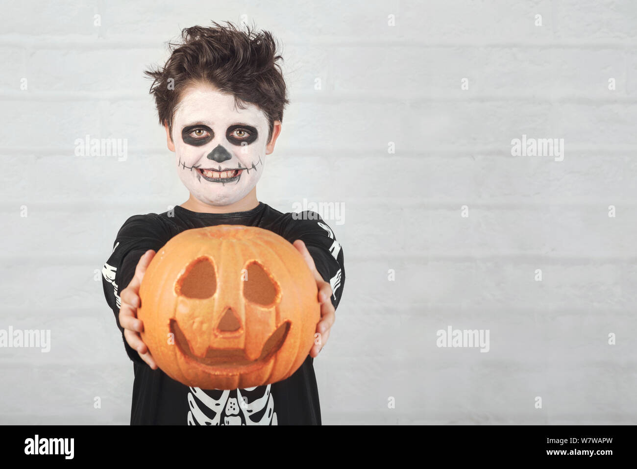 Happy Halloween.divertente bambino in un costume di scheletro con zucca di Halloween contro Sfondo mattone Foto Stock