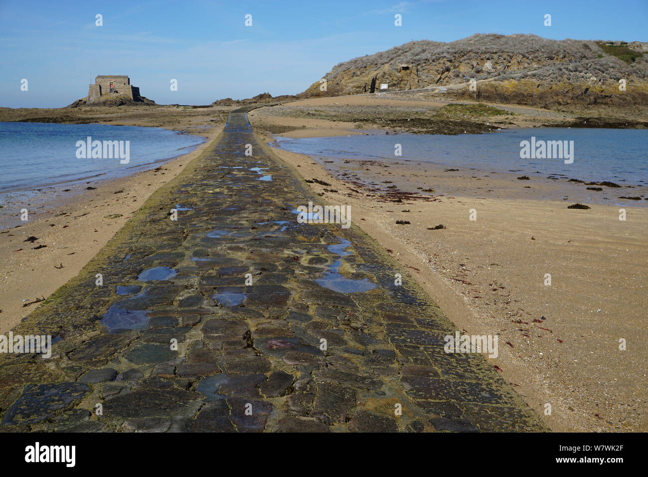 Pietra vecchia strada di accesso a un antico fortilizio a bassa marea e una piccola isola in Bretagna, Francia Foto Stock