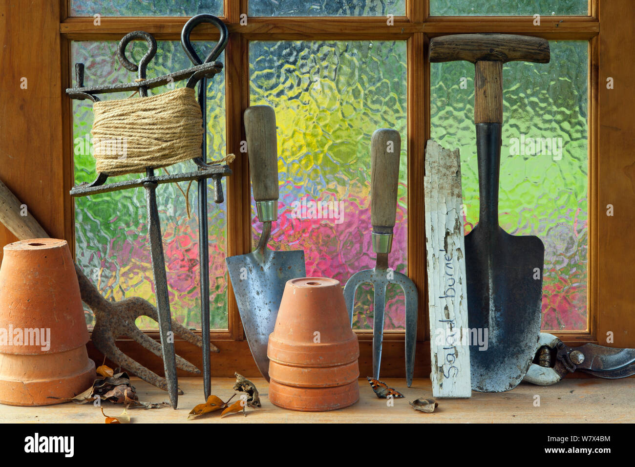 Potting Shed finestra con vasi di fiori, lato forche, stringa e cazzuola sul davanzale. Foto Stock