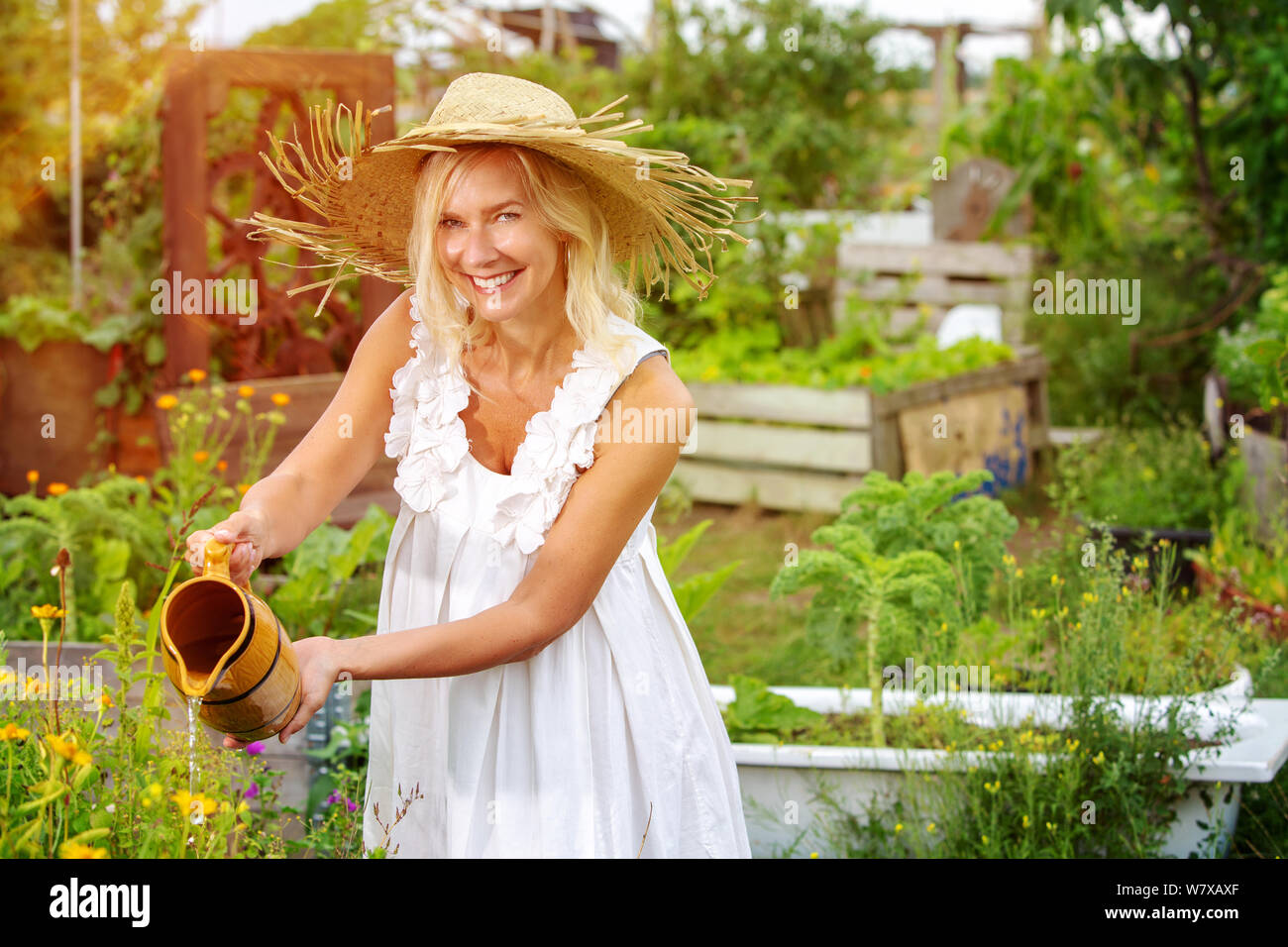Bella donna bionda in abito bianco fiori di irrigazione in giardino Foto Stock