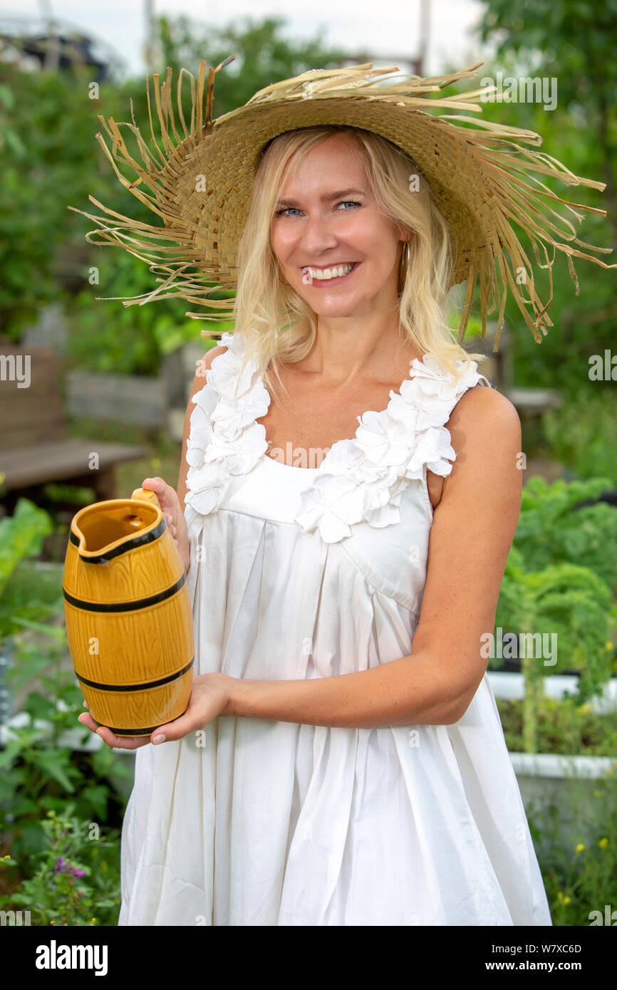 Bella donna bionda in abito bianco fiori di irrigazione in giardino Foto Stock